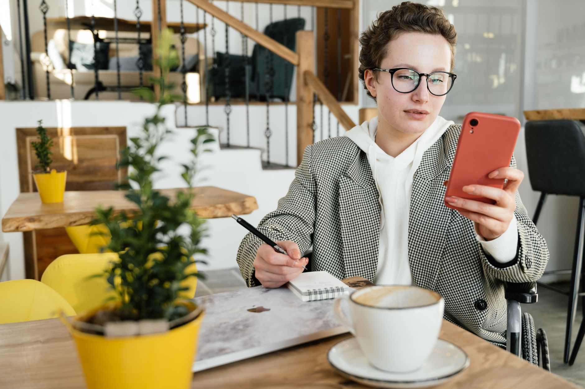 A person jotting notes beside their phone at a cafe table